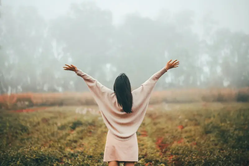 A person with arms raised in a misty meadow