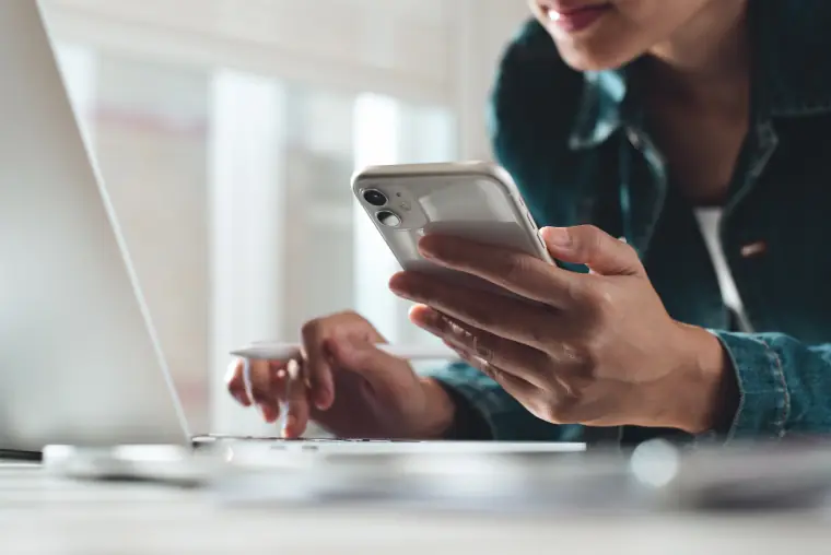 A person using a phone beside a laptop